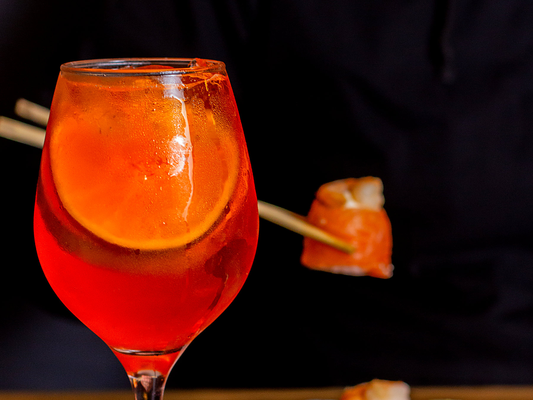 Drink autoral servido em taça com rodela de laranja, à mesa do Himeji